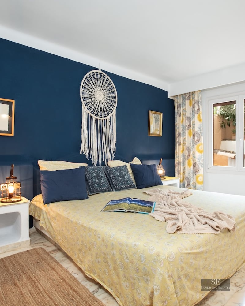 Bedroom featuring a large bed, navy blue accent wall with a dreamcatcher, and polished marble flooring.