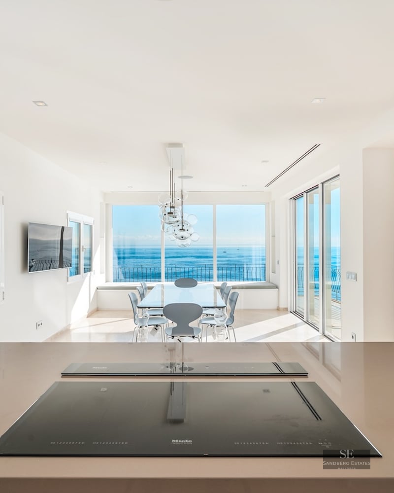 Close-up of a sleek kitchen counter with an induction hob, looking out towards a dining area and a wide blue sea view.