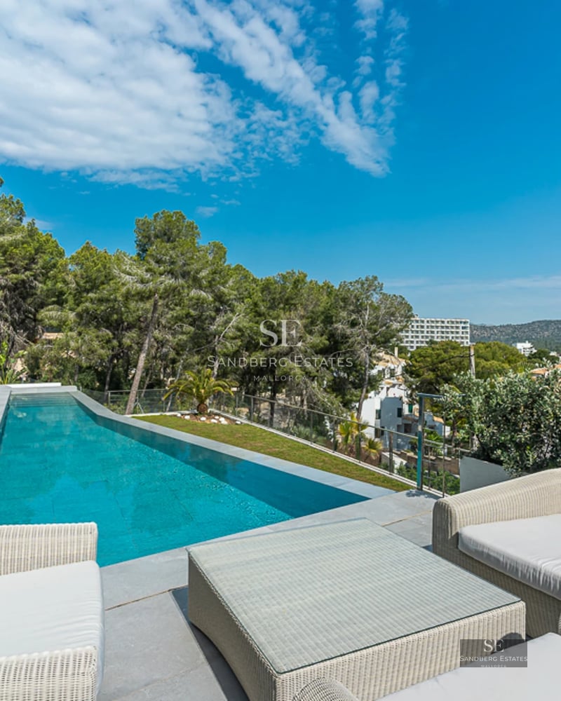 Exterior view of a modern villa featuring an infinity pool, manicured lawn, and minimalist architecture. Warm lighting and blue sky.