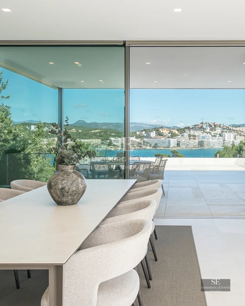 Spacious, bright living room with panoramic windows, light wood flooring and modern furniture. Overlooking garden and pool. Elegant and minimalist design.