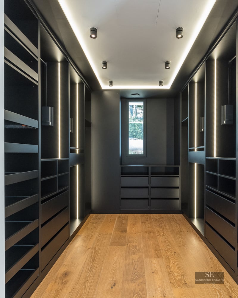 Sleek black walk-in closet with integrated LED lighting and light wood floors.