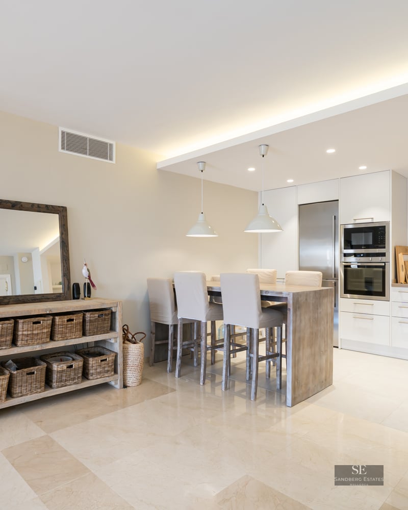 Bright modern kitchen with white cabinets, stainless steel appliances, and a wooden dining island with high chairs.
