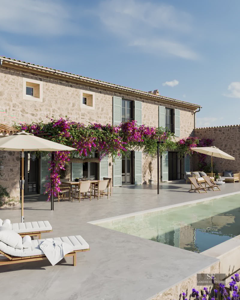 Large swimming pool next to a traditional stone villa with purple bougainvillea flowers and white sun loungers.