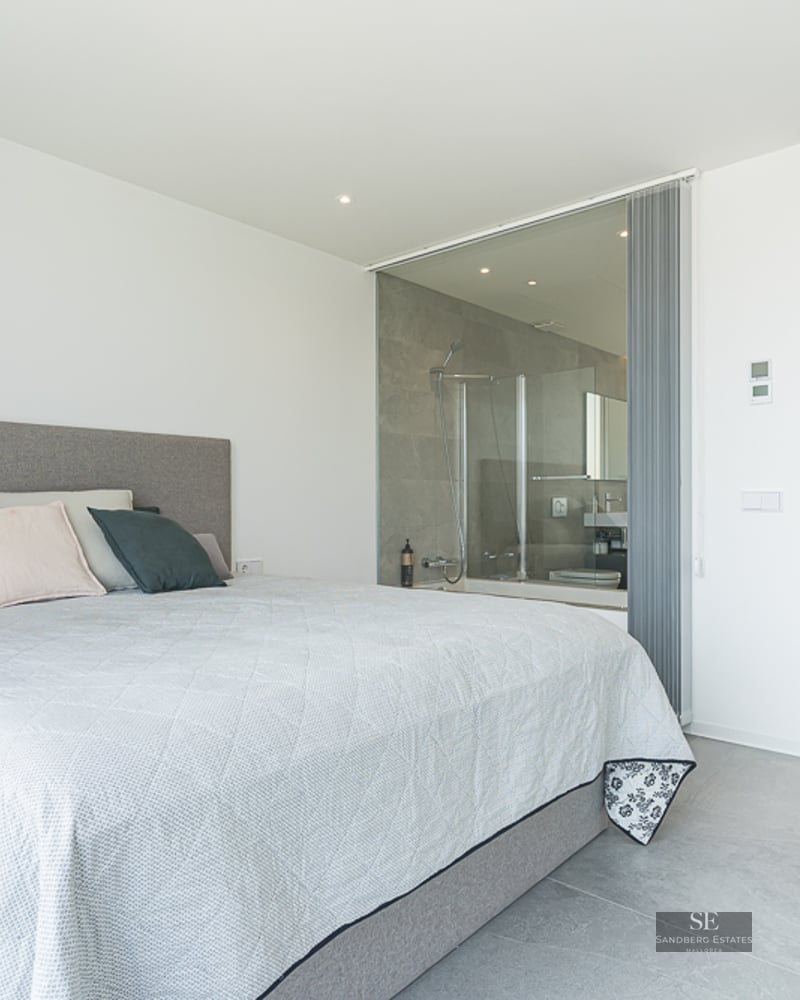Minimalist master bedroom with a large bed and a glass-enclosed ensuite bathroom featuring a walk-in shower.