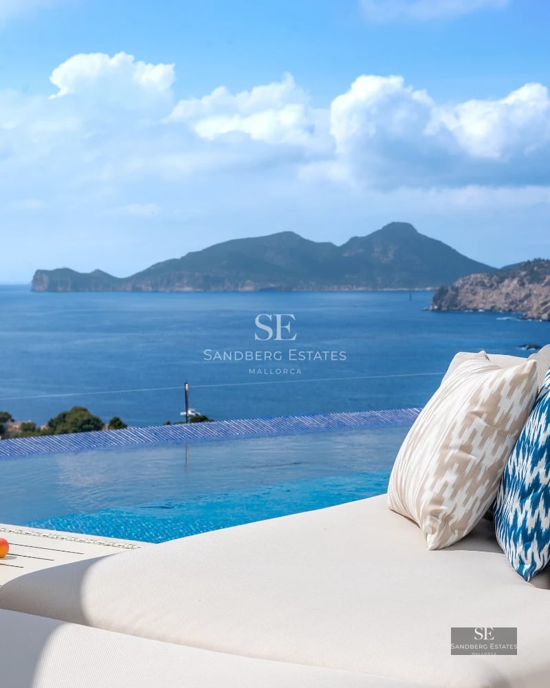 Spacious balcony with light wood flooring, glass railing, sea view, and modern outdoor furniture. Abundant natural lighting.