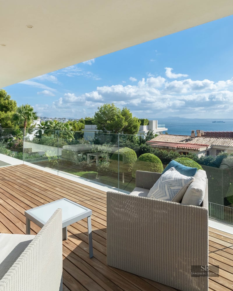 Modern terrace with wooden decking, white sofas, and glass railing featuring panoramic sea views.