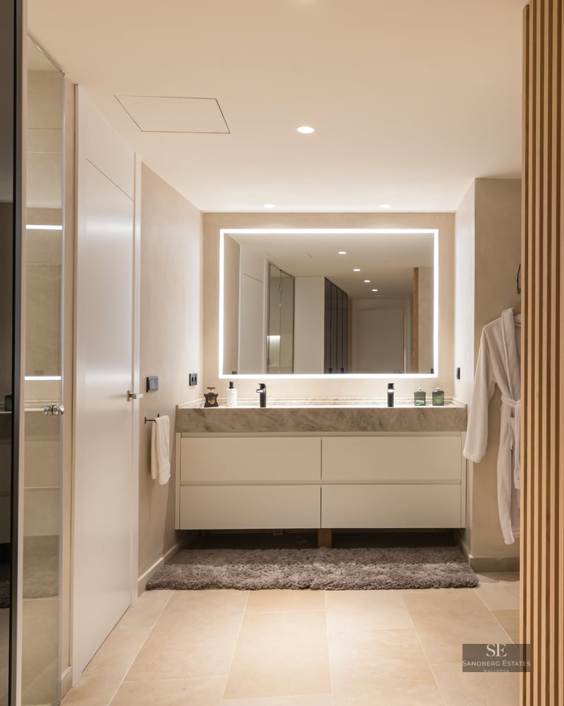 Modern bathroom featuring a marble double vanity, large backlit LED mirror, and vertical wood slat wall.