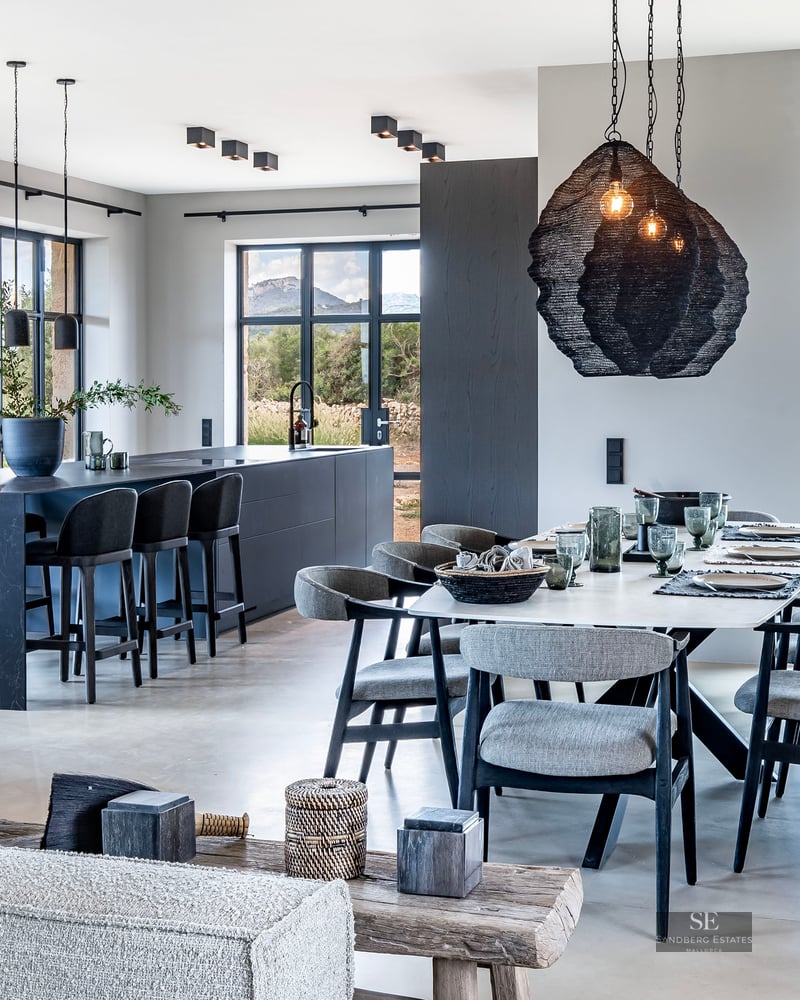 Elegant dining area featuring a long table, dark kitchen island, and large windows with countryside views.
