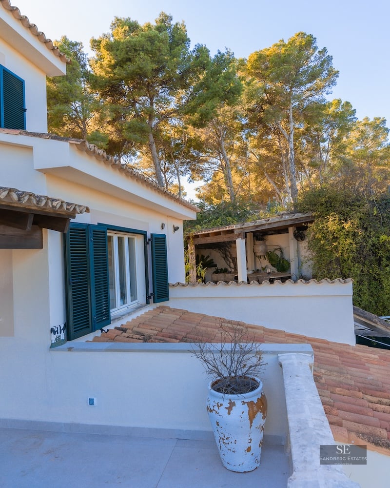 White Mediterranean villa exterior with terracotta roof tiles, dark green shutters, and large rustic white planters.