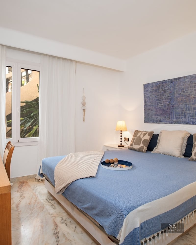 White bedroom featuring a blue bed, wooden desk, and veined marble floors under warm ambient lighting.