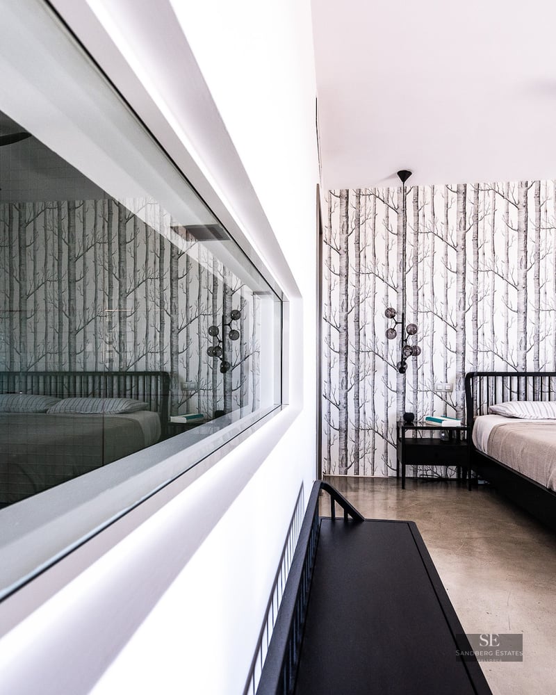 Modern bedroom featuring a black bed, birch tree wallpaper, and a large internal glass window reflecting the space.