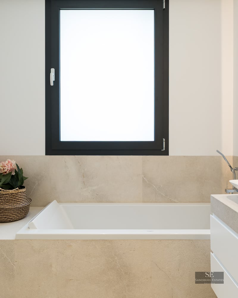 Minimalist bathroom featuring a white built-in tub, vessel sink on a stone vanity, and a black-framed window.