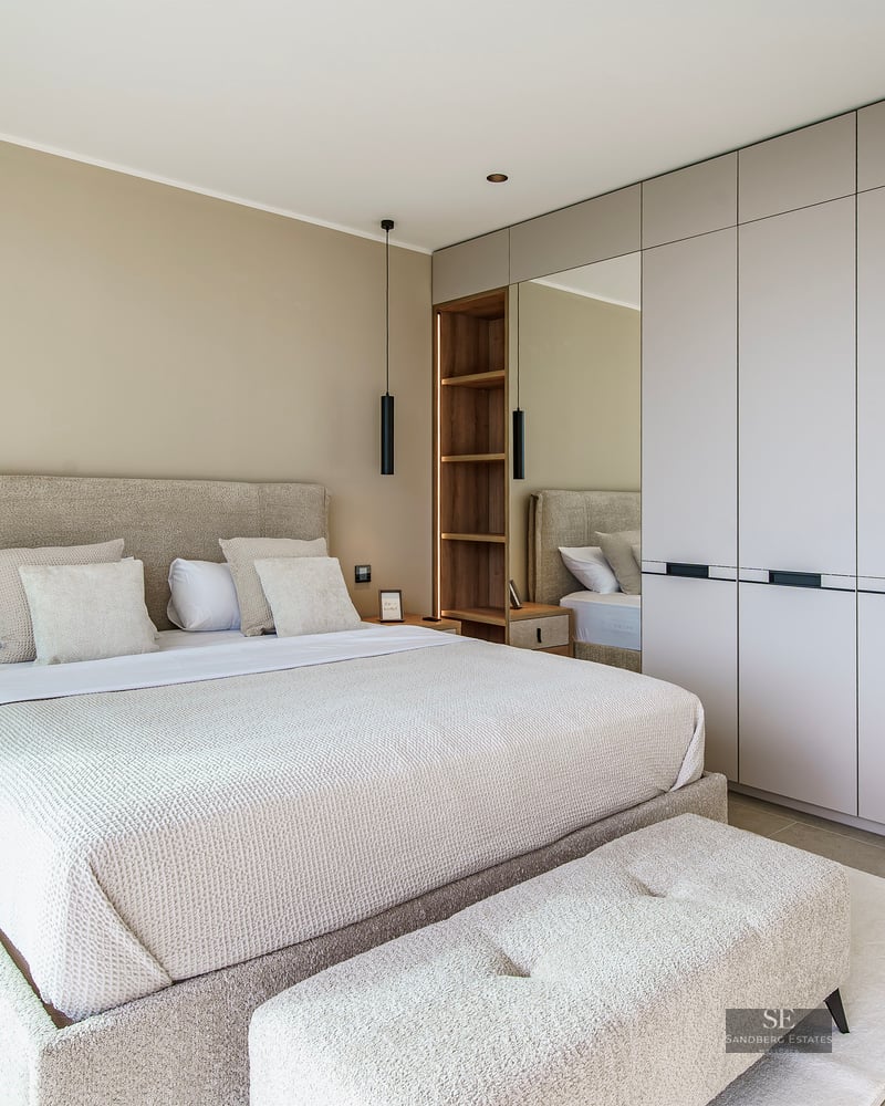 Modern bedroom featuring a large beige upholstered bed, minimalist built-in closets, and elegant black pendant lighting.
