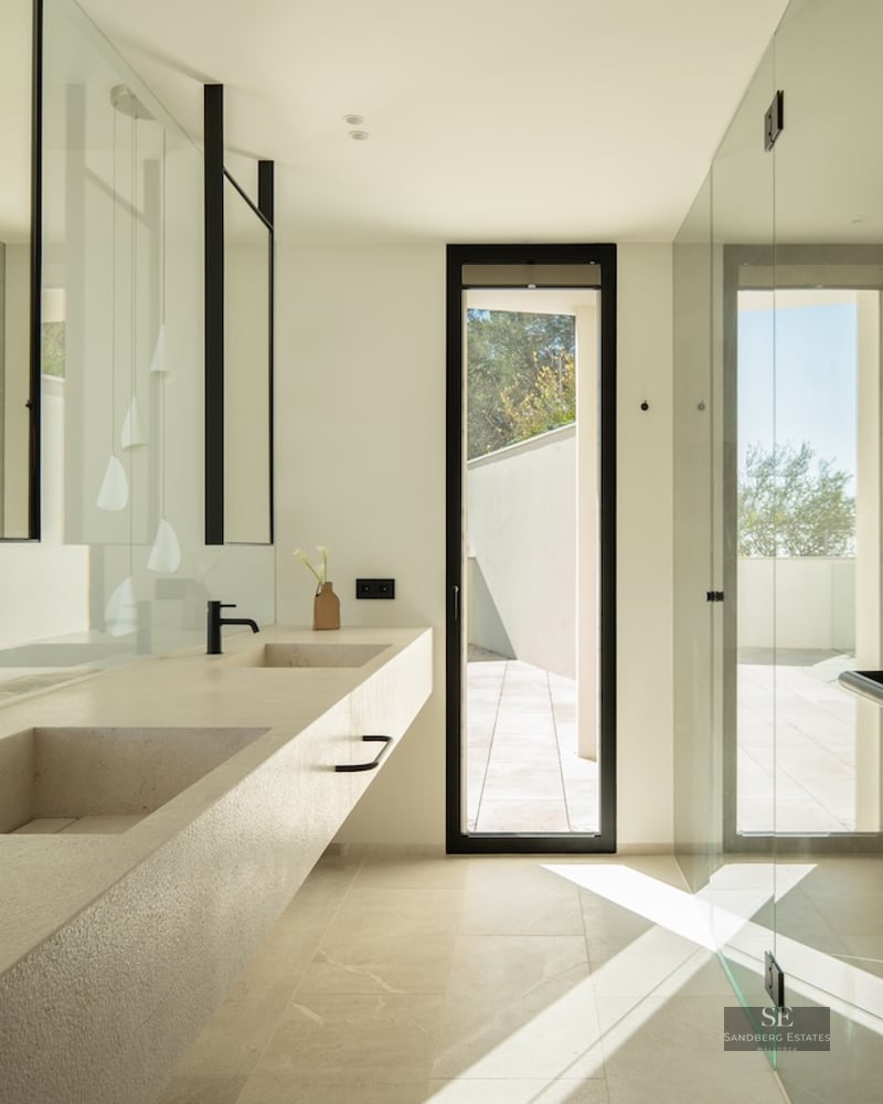 Modern bathroom featuring a long stone double vanity with black faucets, large mirrors, and natural light from a window.
