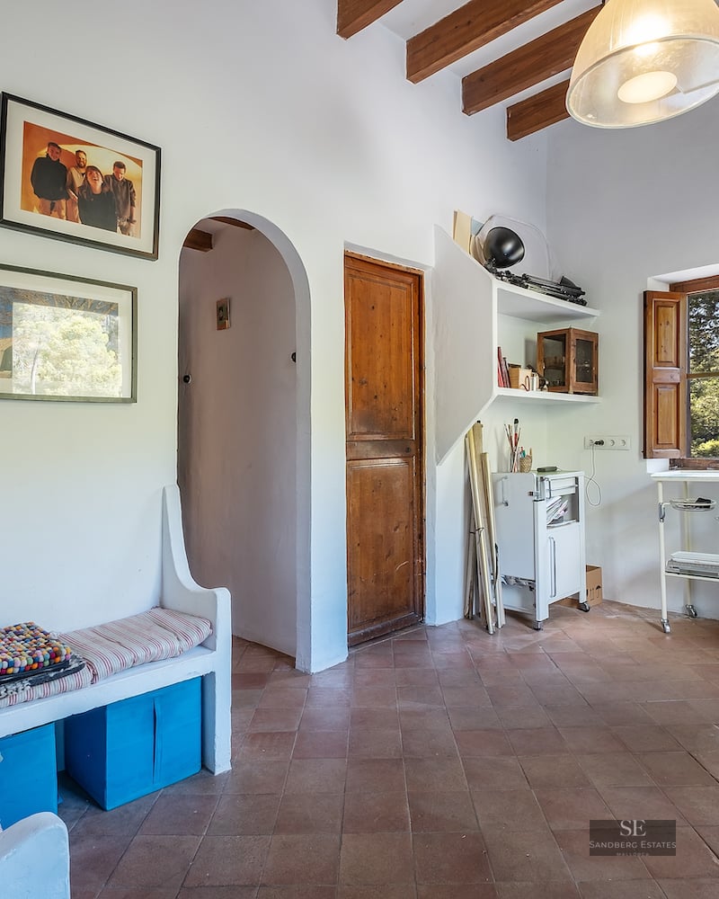 Interior room featuring terracotta floor tiles, exposed wooden ceiling beams, white walls, and a built-in bench.