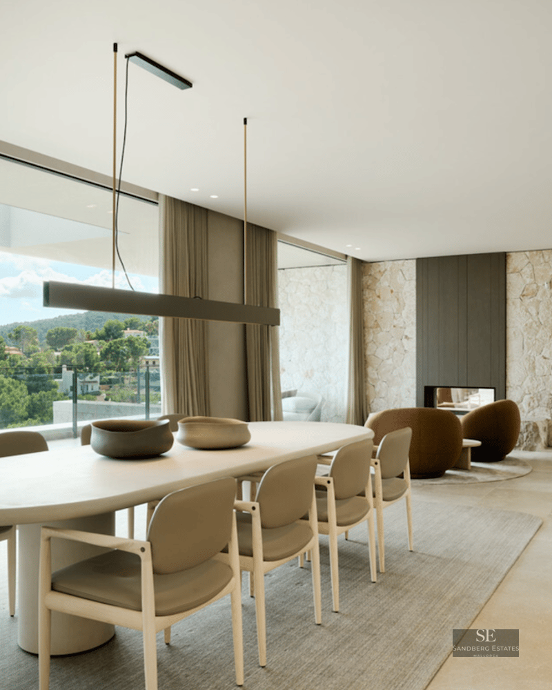 Modern dining area featuring an oval table, stone feature walls, and floor-to-ceiling windows overlooking a lush landscape.
