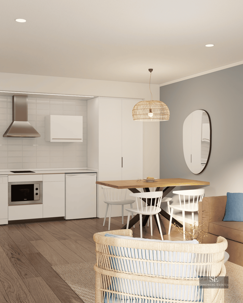 Salon lumineux avec cuisine intégrée, table à manger en bois et canapé beige avec coussins bleus.