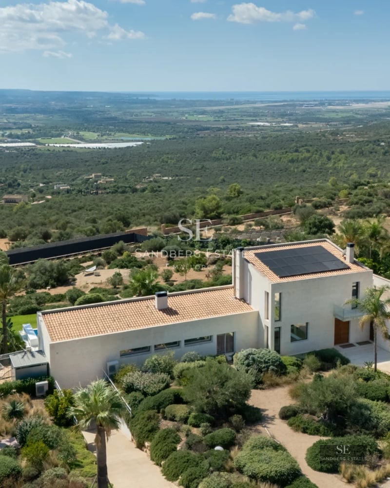 View of infinity pool and lush garden. Modern architecture with large windows and furnished terrace. Elegant and sophisticated design.