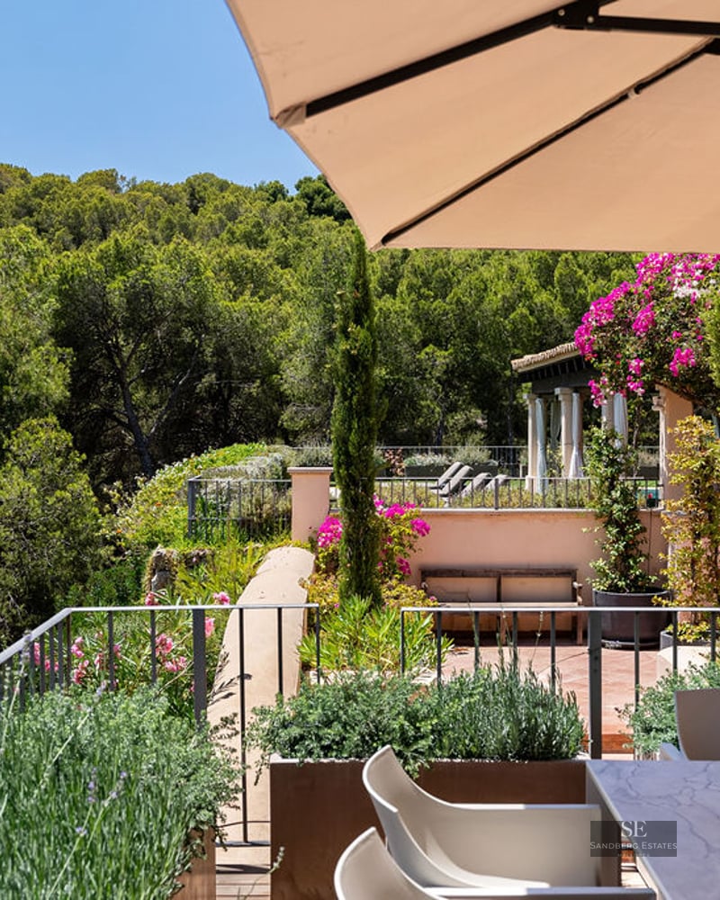 Terrace with a marble dining table and sun umbrella overlooking a lush green pine forest under a clear blue sky.