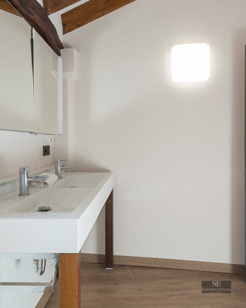Bathroom featuring a white double sink vanity, exposed wooden ceiling beams, a dark grey door, and a mirror cabinet.