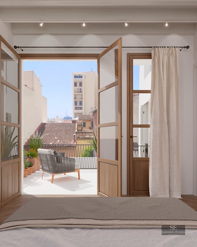 Modern bedroom view through open wooden doors to a sunny terrace with city views and outdoor seating.