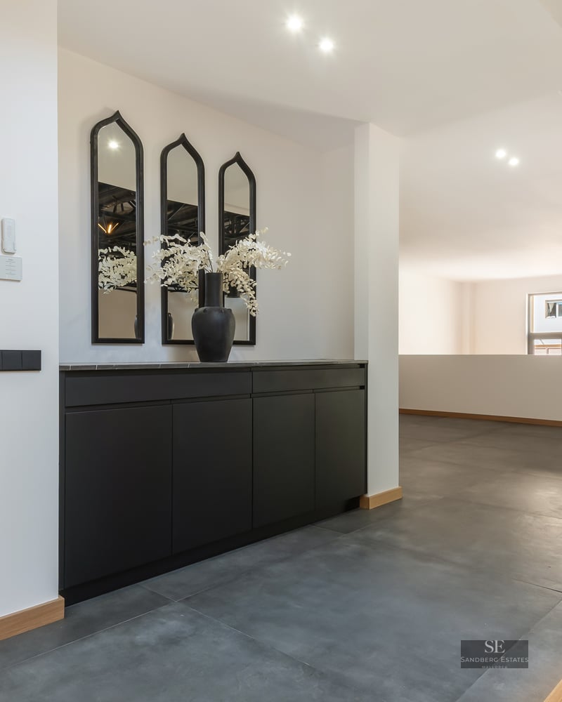 Modern hallway with black cabinetry, arched mirrors, grey tile floors, and a glass railing overlooking the lower floor.