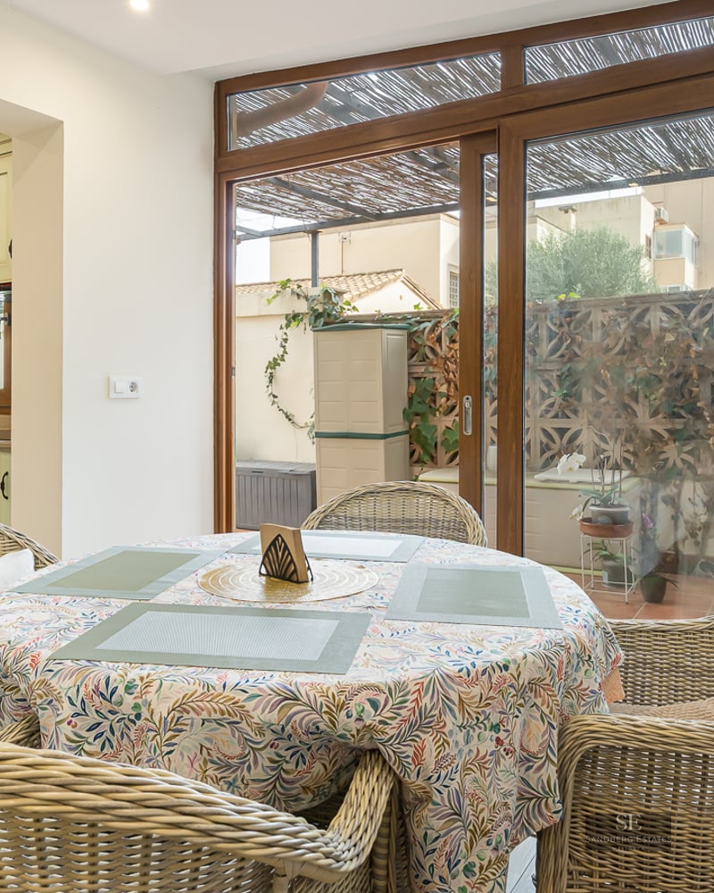Dining table with wicker chairs next to a sage green kitchen and large sliding glass doors.
