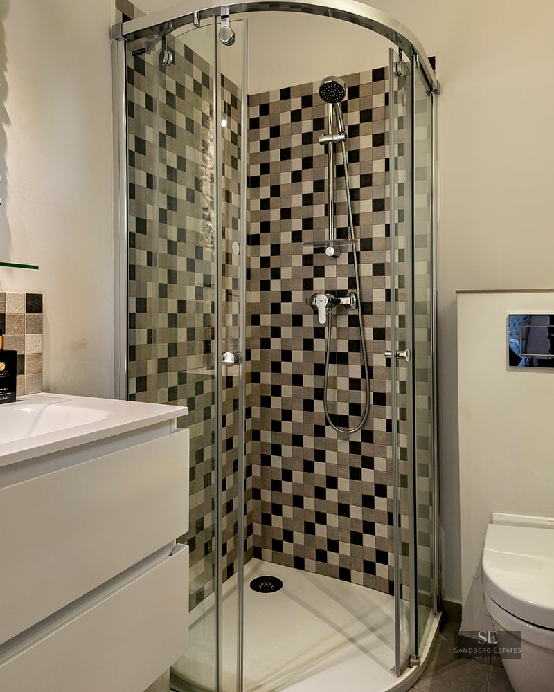 Modern bathroom featuring a curved glass corner shower with checkered tiles, a white vanity, and an ornate mirror.