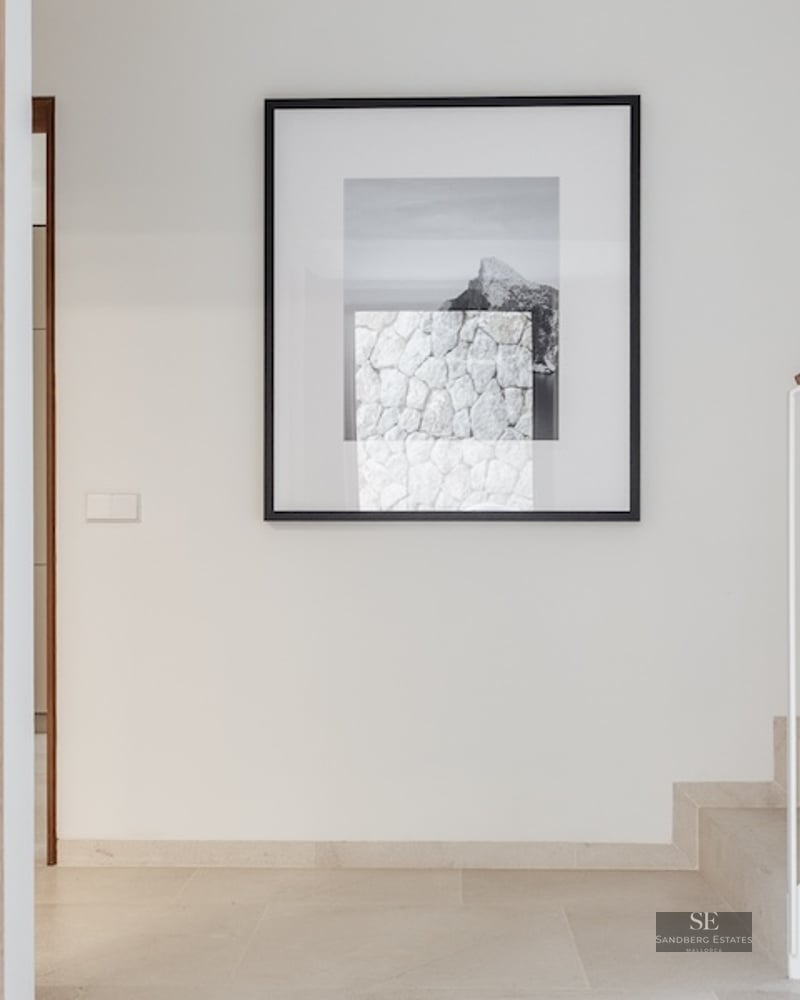 Minimalist hallway with stone stairs, a wooden handrail, and a large framed artwork on a white wall.