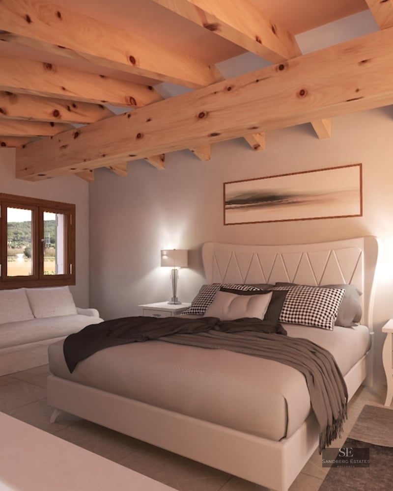 Bedroom with large bed, exposed wooden ceiling beams, white sofa, and windows looking out to the countryside.