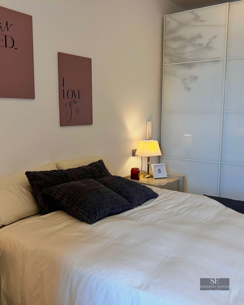 Bedroom featuring a large bed, grey textured pillows, pink wall art, and a large white sliding-door wardrobe.