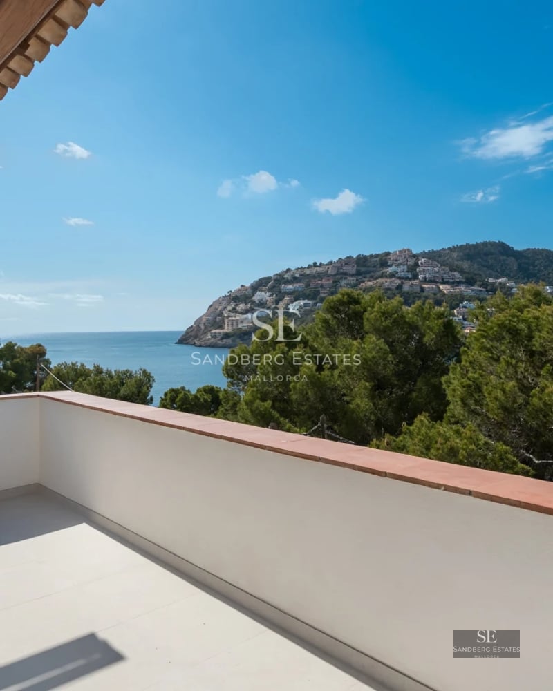 Spacious balcony with sea view, modern furniture, glass railing and wooden floor, part of a luxury apartment.