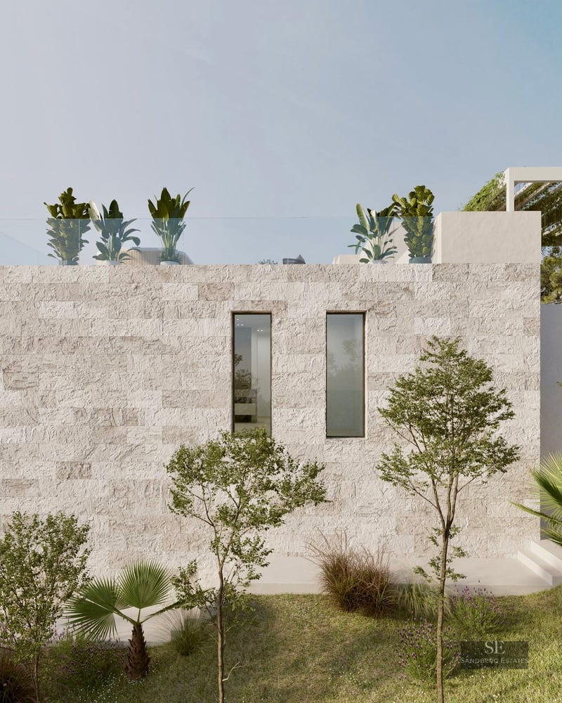 Side view of a modern luxury villa with textured stone walls, rooftop terrace, and Mediterranean landscaping overlooking the sea.