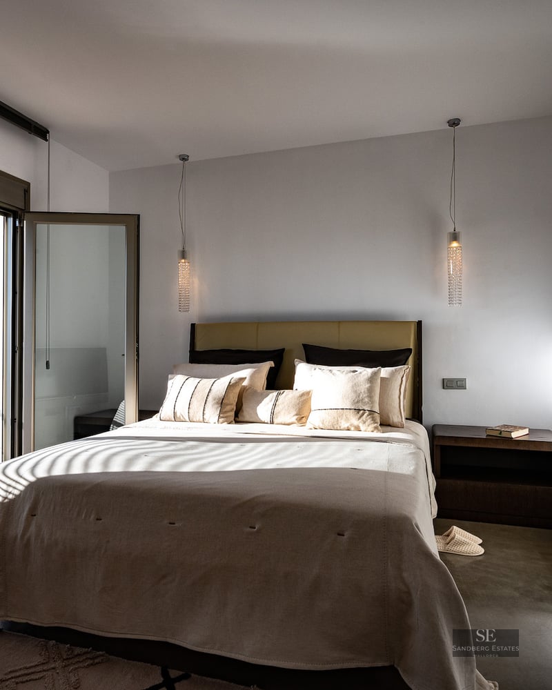 Bright bedroom featuring a large bed, polished concrete floors, and glass doors opening to a sunny private terrace.