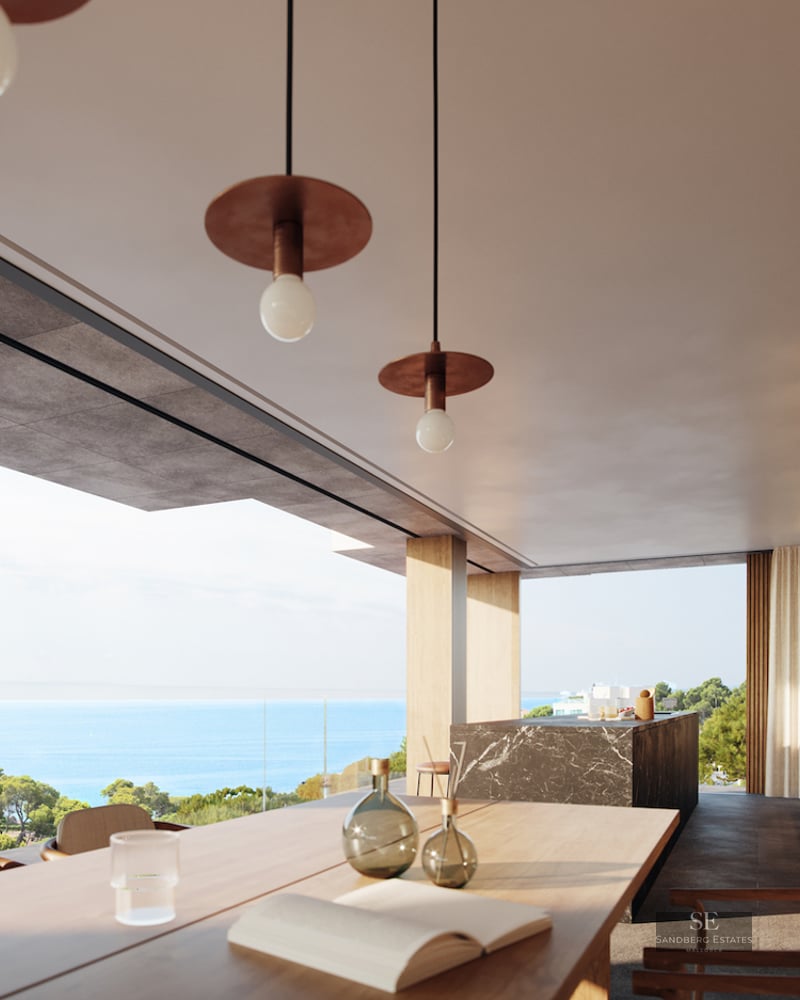 Interior of a luxury dining room with a wooden table and marble island overlooking the Mediterranean sea and pine trees.