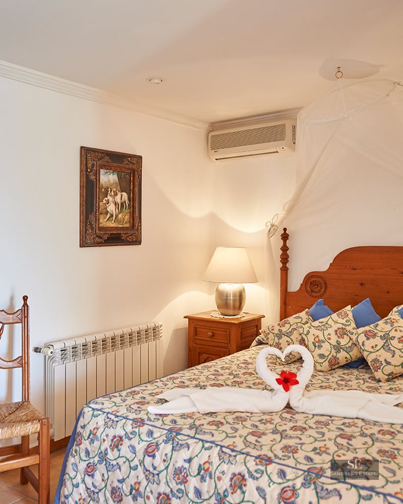 Cozy bedroom with a wooden bed, white mosquito net canopy, floral bedding, and rustic wooden furniture.