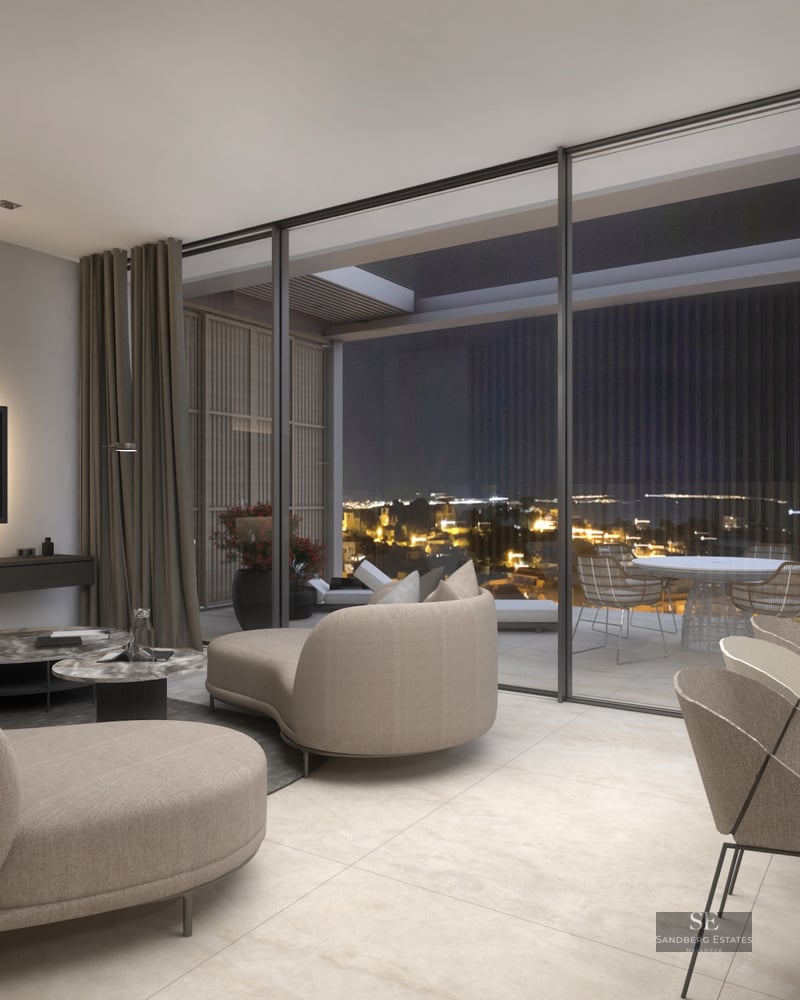 Luxury living room with beige sofas, large glass doors, and a terrace overlooking city lights at night.
