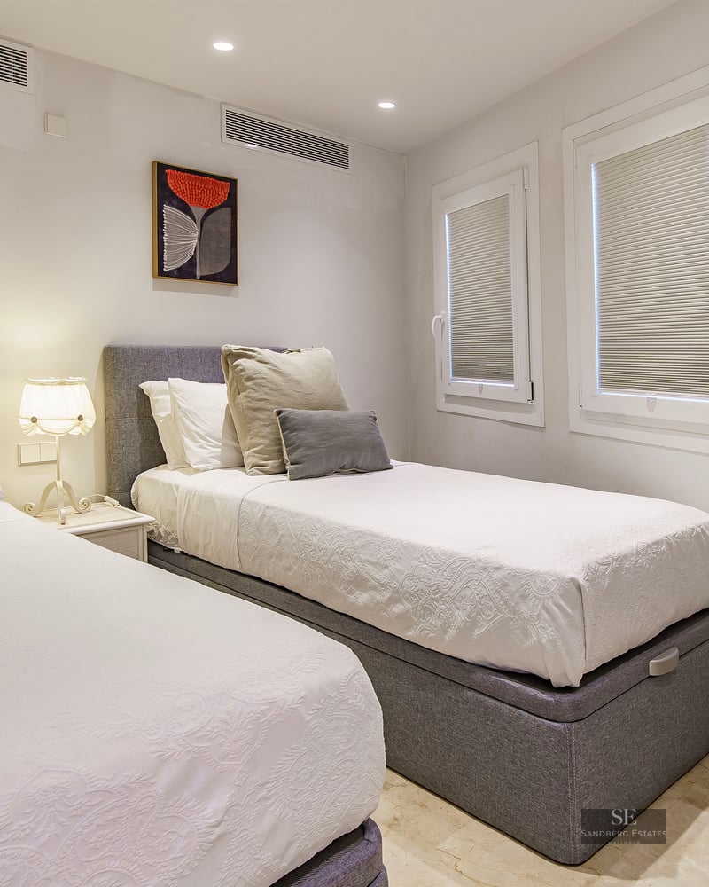 Bedroom with two single beds, grey headboards, white linens, and contemporary wall art.