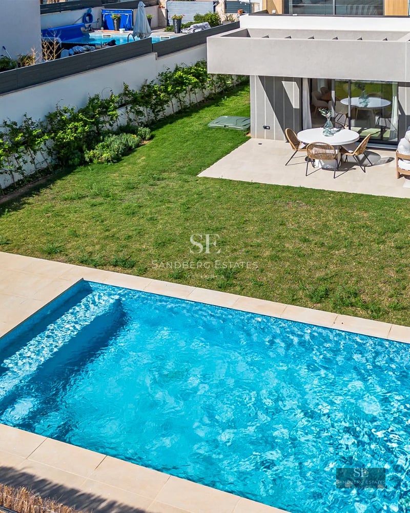View of infinity pool with wide sun loungers, surrounded by lush greenery. Modern architecture and impeccable exterior design.