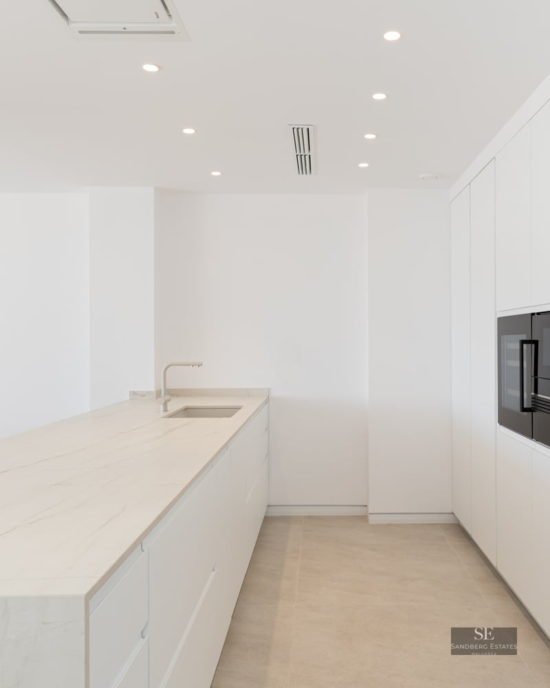 Modern minimalist white kitchen featuring a large marble island and high-end integrated appliances.