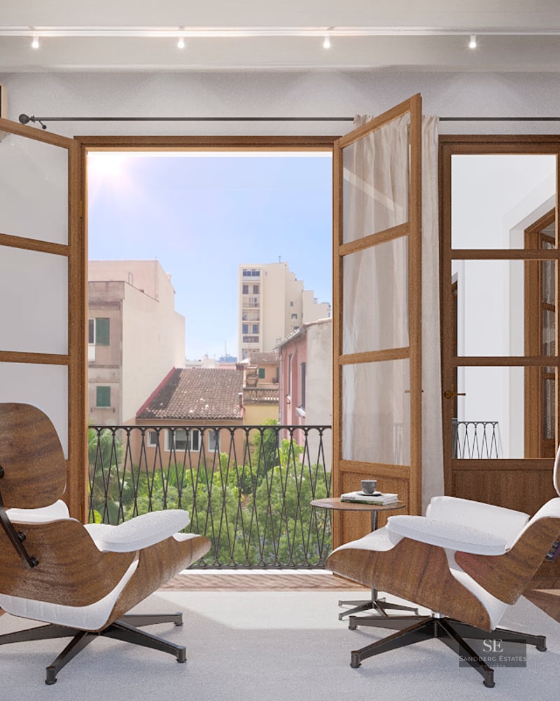 Bright living room with two Eames chairs facing an open balcony overlooking a Mediterranean city.
