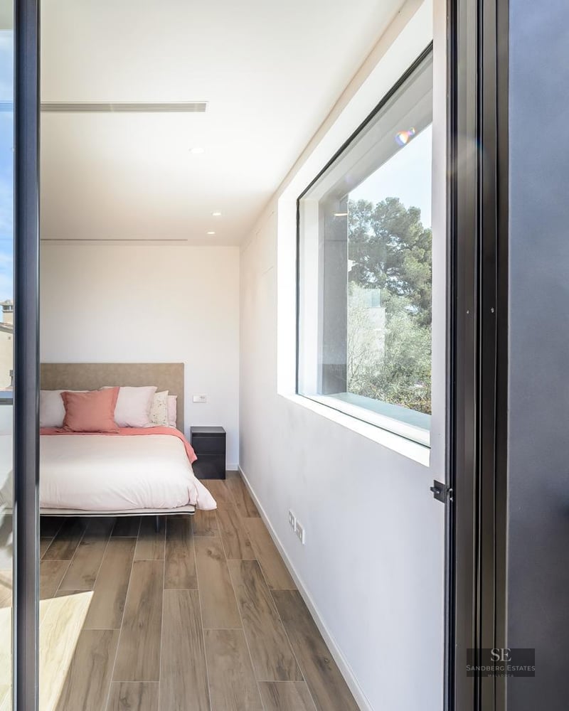 Modern bedroom with wood floors, a bed with pink pillows, and large windows overlooking green trees.
