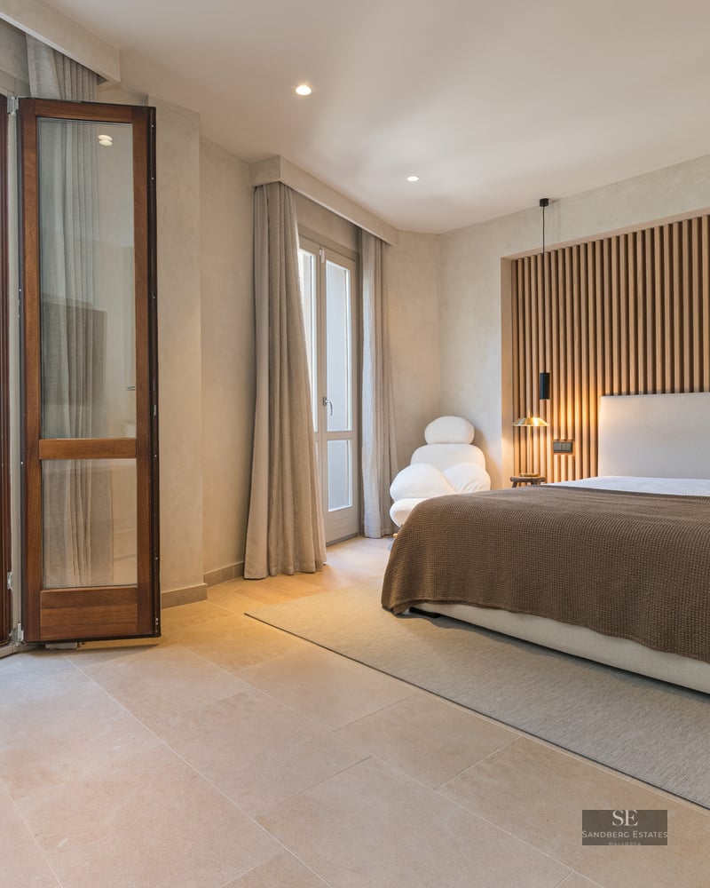 Modern master bedroom with wooden slat wall and large glass doors opening to a sunny private terrace.