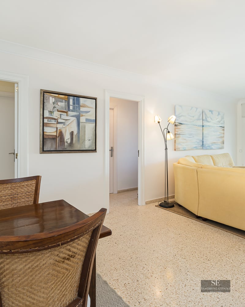 Open living space with a cream leather sofa, wooden dining set, and large glass doors revealing a mountain landscape.