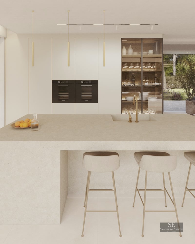 A minimalist modern kitchen featuring a large stone central island, beige bar stools, and natural stone wall accents.