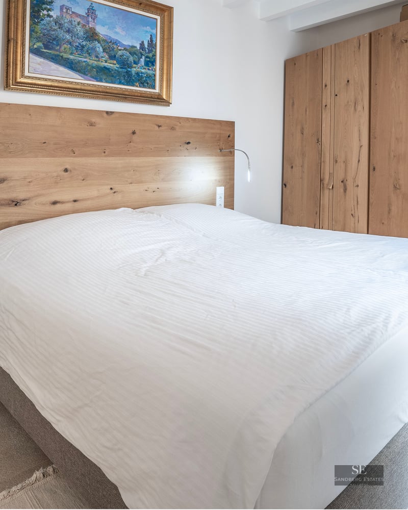 Chambre moderne avec grand lit, tête de lit et armoire en bois clair et un tableau classique.