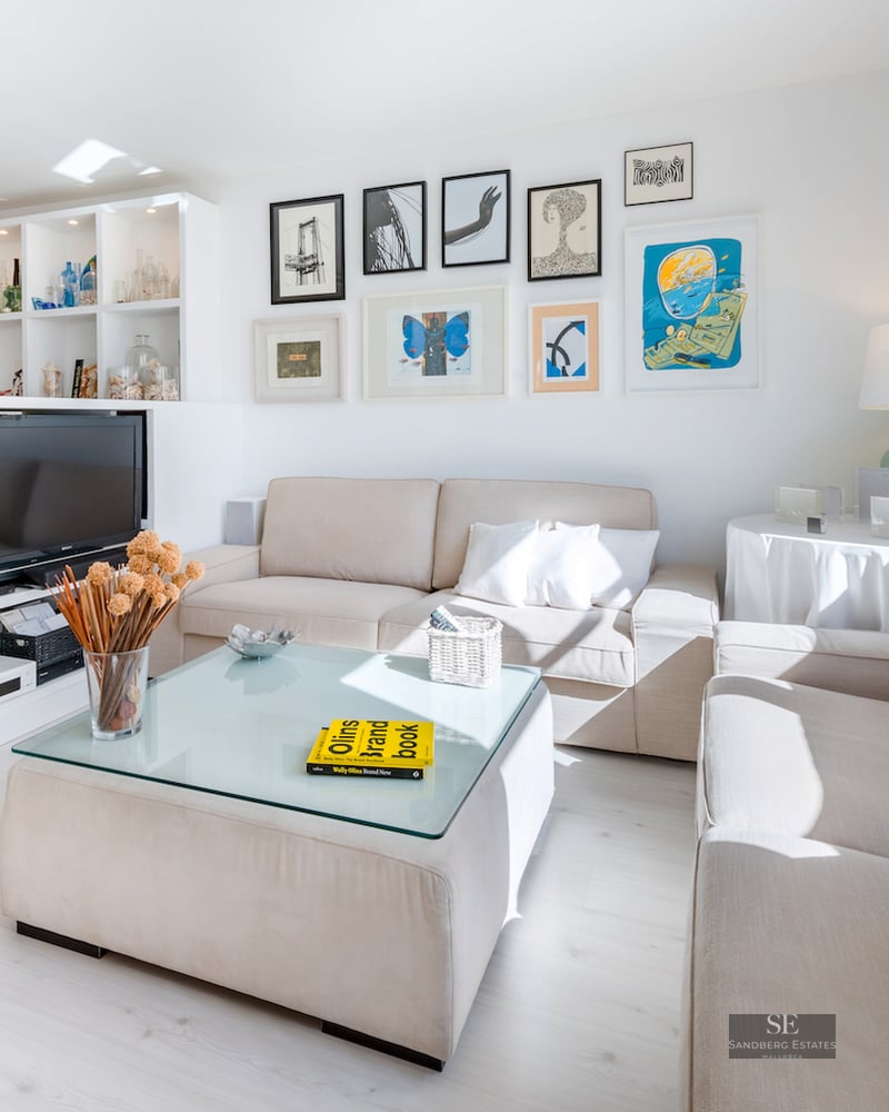 Spacious living room featuring beige sofas, a glass-topped ottoman coffee table, and an extensive art gallery wall.