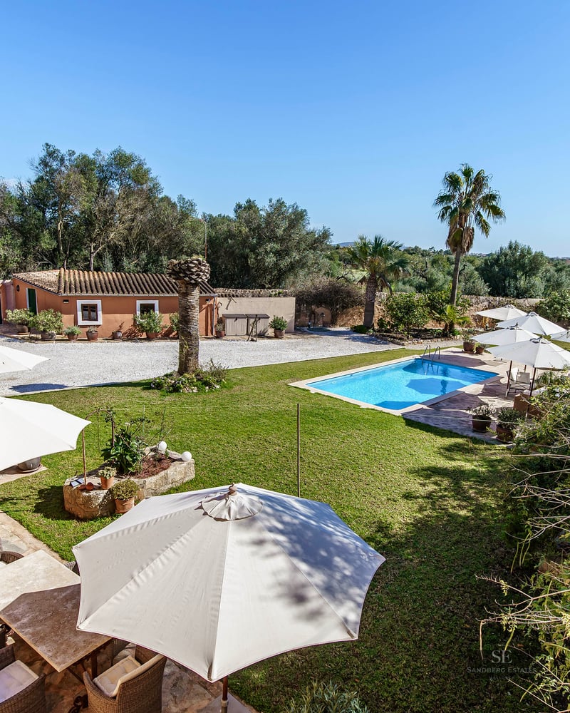 Rectangular swimming pool surrounded by green lawn, sun umbrellas, and a stone terrace at a Mediterranean estate.
