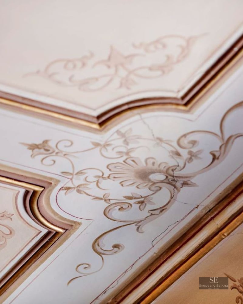 Close-up of ornate ceiling molding with hand-painted floral filigree in cream and gold.