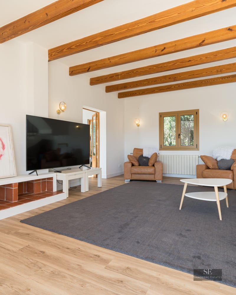 Cozy living room featuring exposed wood beams, a black wood-burning stove, tan leather sofas, and a large TV.